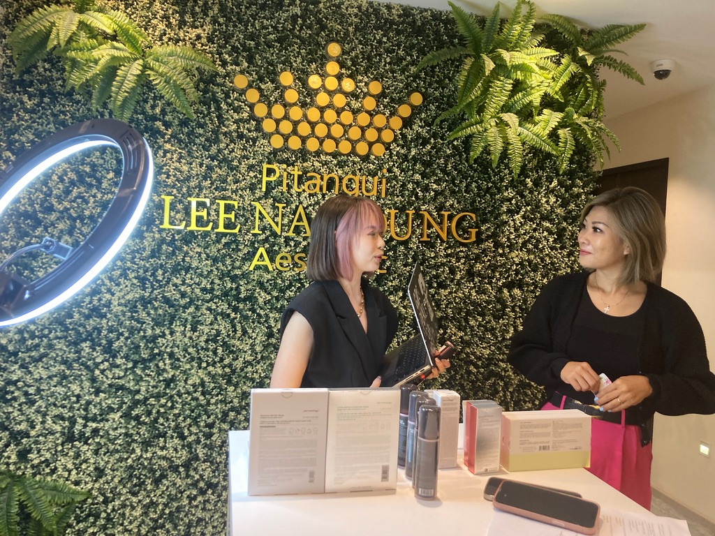 Two presenters discussing aesthetic products beside a ring light and product display